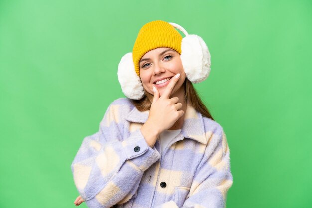 Joven mujer rubia con manguitos de invierno sobre un fondo aislado de croma key sonriendo