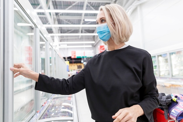 Joven mujer rubia con máscara en un supermercado. Pandemia de coronavirus.