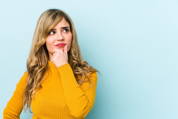 Joven mujer rubia mirando hacia los lados con expresión dudosa y escéptica