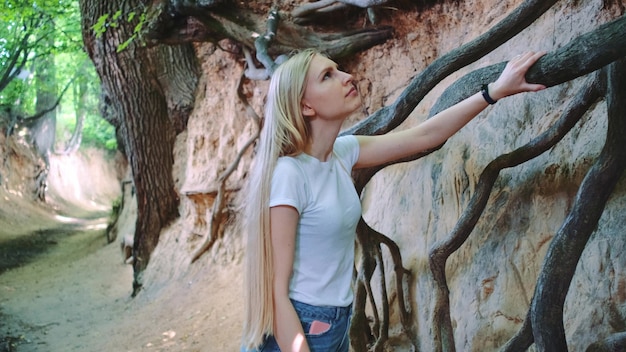 Joven mujer rubia mirando las raíces de los árboles expuestos en el barranco de loess natural