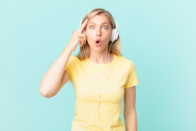 Joven mujer rubia mirando sorprendida, dándose cuenta de un nuevo pensamiento, idea o concepto y escuchando música.