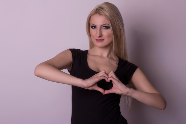 Joven mujer rubia mostrando un corazón por sus dedos