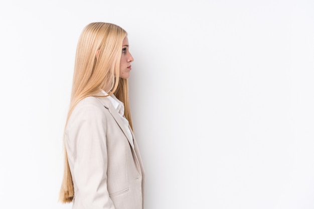 Joven mujer rubia de negocios en la pared blanca mirando hacia la izquierda, de lado plantean.