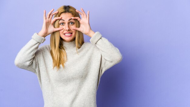 Joven mujer rubia en la pared púrpura manteniendo los ojos abiertos