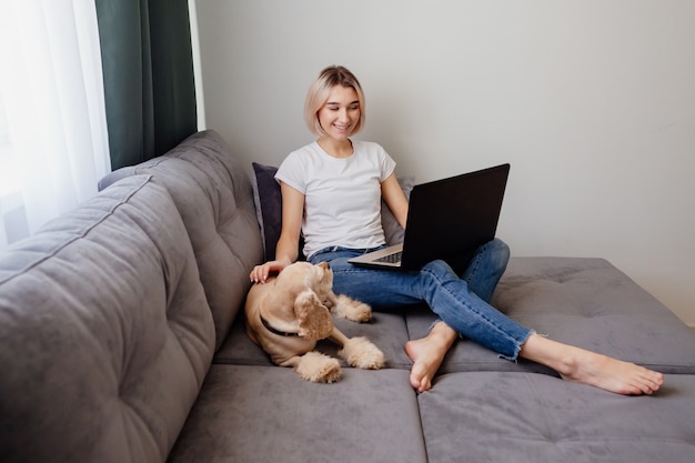 Joven mujer rubia con un perro de aguas sentado en una computadora portátil blogger trabajando en Internet en la oficina en casa