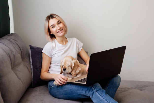 Joven mujer rubia con un perro de aguas sentado en una computadora portátil blogger trabajando en Internet en la oficina en casa