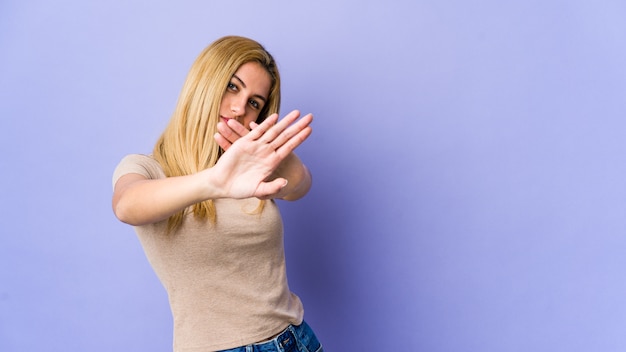 Joven mujer rubia de pie con la mano extendida mostrando la señal de stop, impidiéndote.