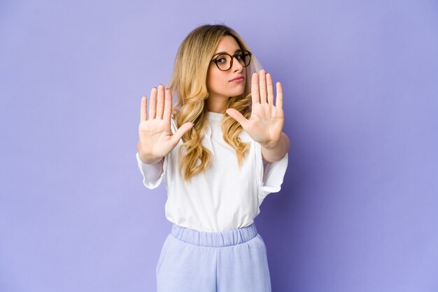 Joven mujer rubia de pie con la mano extendida mostrando la señal de stop