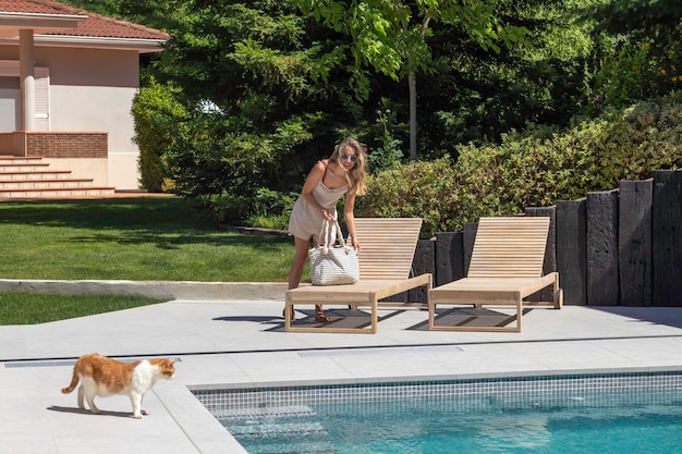 Joven mujer rubia en la piscina en un salón de sol con su gato blanco y naranja mirando el agua