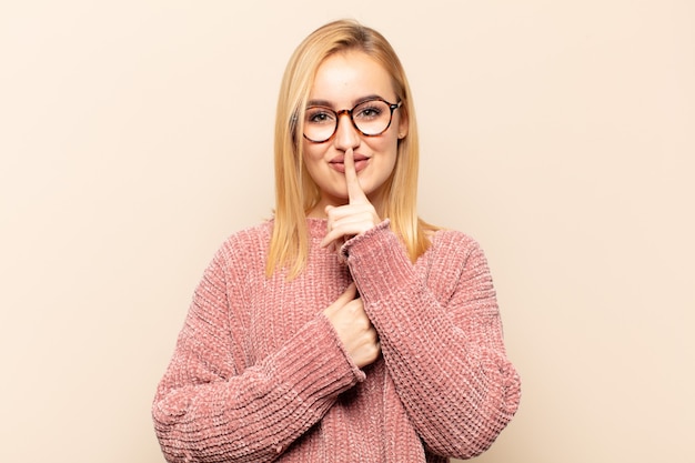 Joven mujer rubia que parece seria y cruzada con el dedo presionado a los labios exigiendo silencio o silencio, manteniendo un secreto