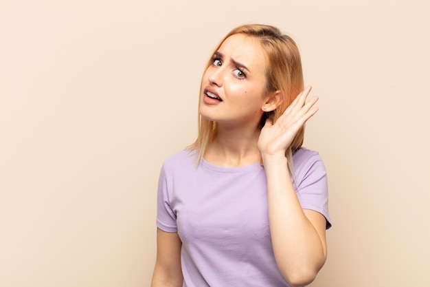 Joven mujer rubia que parece seria y curiosa, escuchando, tratando de escuchar una conversación secreta o chismes, escuchando a escondidas