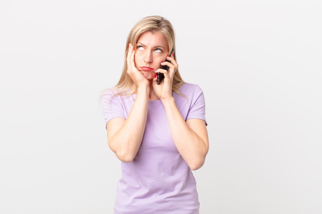 Joven mujer rubia que se siente aburrida, frustrada y con sueño después de un cansado y llamando con un teléfono inteligente.