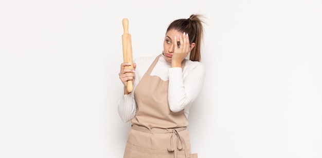 Joven mujer rubia que se siente aburrida, frustrada y con sueño después de una tarea aburrida, aburrida y tediosa, sosteniendo la cara con la mano