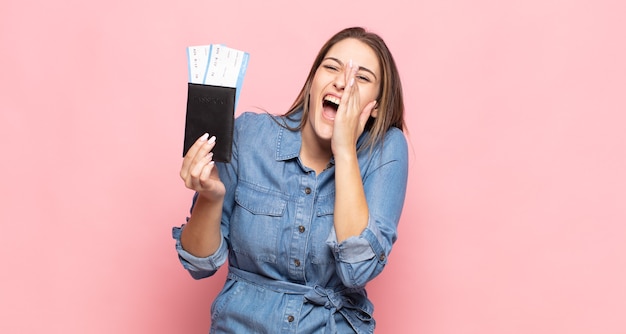 Joven mujer rubia que se siente feliz, emocionada y positiva, dando un gran grito con las manos al lado de la boca, gritando