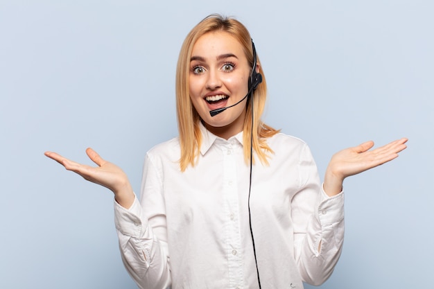 Joven mujer rubia que se siente feliz, emocionada, sorprendida o conmocionada, sonriendo y asombrada por algo increíble