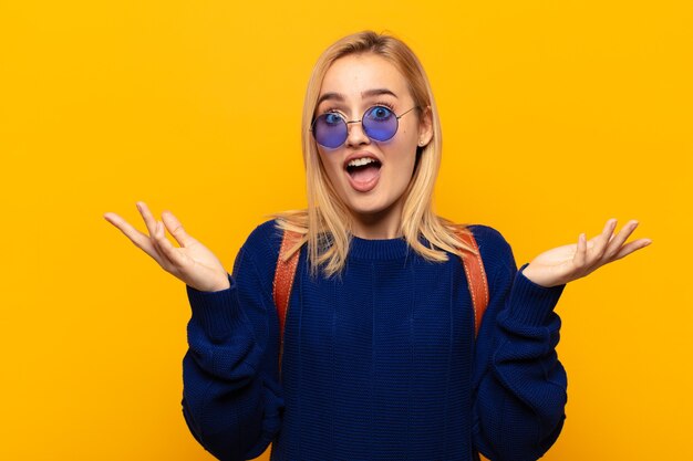 Joven mujer rubia que se siente feliz, emocionada, sorprendida o conmocionada, sonriendo y asombrada por algo increíble