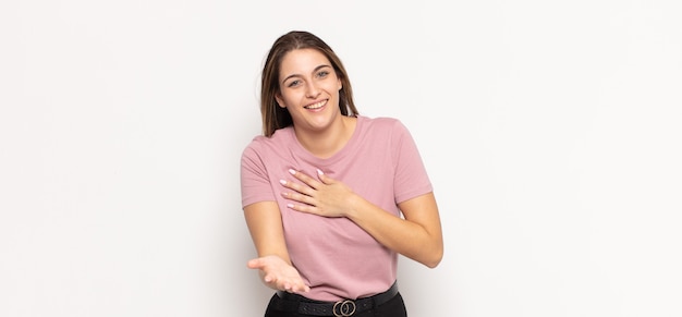 Joven mujer rubia que se siente feliz y enamorada, sonriendo con una mano al lado del corazón y la otra estirada al frente