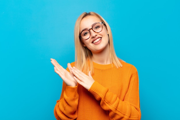 Joven mujer rubia que se siente feliz y exitosa, sonriendo y aplaudiendo, felicitando con un aplauso