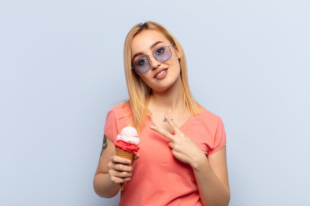 Joven mujer rubia que se siente feliz, positiva y exitosa, con la mano haciendo forma de v sobre el pecho, mostrando la victoria o la paz