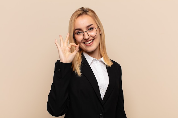 Joven mujer rubia que se siente feliz, relajada y satisfecha, mostrando aprobación con gesto bien, sonriendo