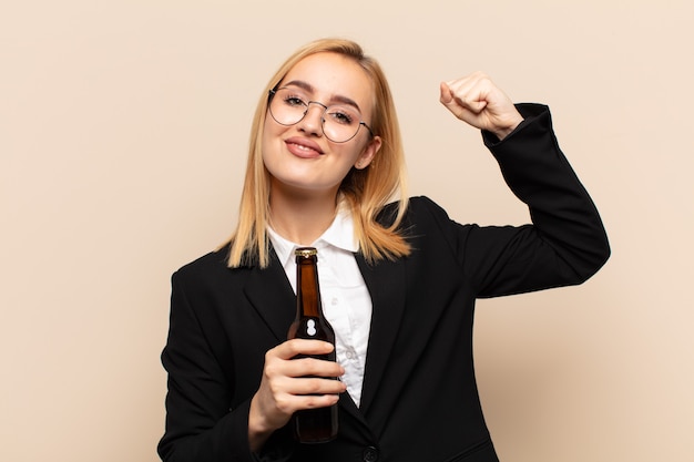 Joven mujer rubia que se siente feliz, satisfecha y poderosa, flexionando el ajuste y los bíceps musculosos, luciendo fuerte después del gimnasio