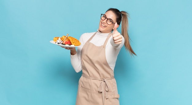 Joven mujer rubia que se siente orgullosa, despreocupada, segura y feliz, sonriendo positivamente con los pulgares hacia arriba