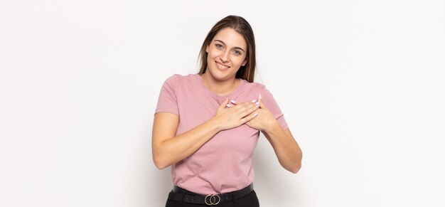 Joven mujer rubia que se siente romántica, feliz y enamorada, sonriendo alegremente y tomados de la mano cerca del corazón