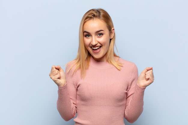 Joven mujer rubia que se siente sorprendida, emocionada y feliz, riendo y celebrando el éxito, diciendo ¡guau!