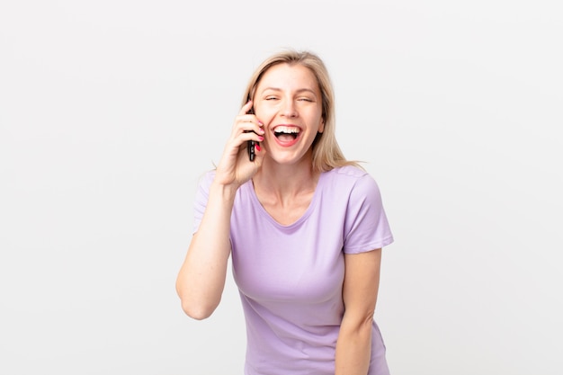 Joven mujer rubia riendo a carcajadas de una broma hilarante y llamando con un teléfono inteligente