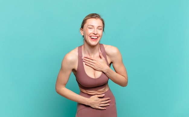 Joven mujer rubia riendo a carcajadas de una broma hilarante, sintiéndose feliz y alegre, divirtiéndose. concepto de deporte