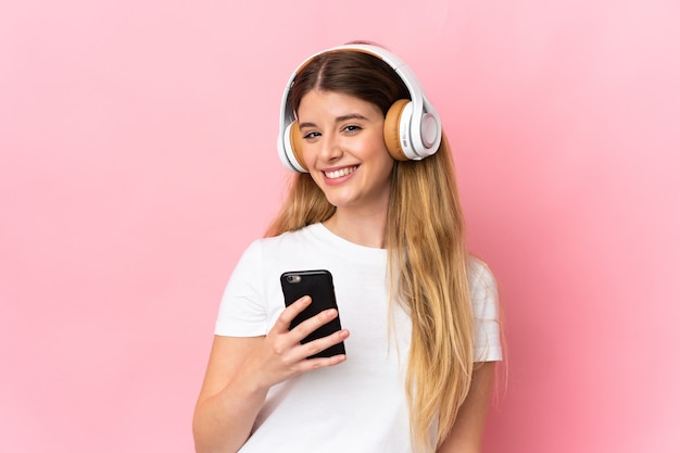 Joven mujer rubia sobre espacio aislado escuchando música con un móvil y mirando al frente