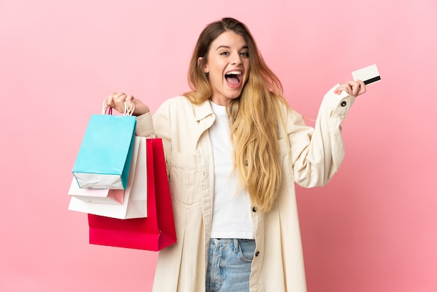 Joven mujer rubia sobre espacio aislado sosteniendo bolsas de compras y sorprendido