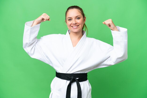 Joven mujer rubia sobre un fondo clave de croma aislado haciendo karate y haciendo un gesto fuerte