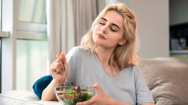 Joven mujer rubia en un sofá con ensalada saludable