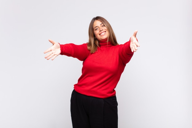 Joven mujer rubia sonriendo alegremente dando un cálido, amable y cariñoso abrazo de bienvenida, sintiéndose feliz y adorable