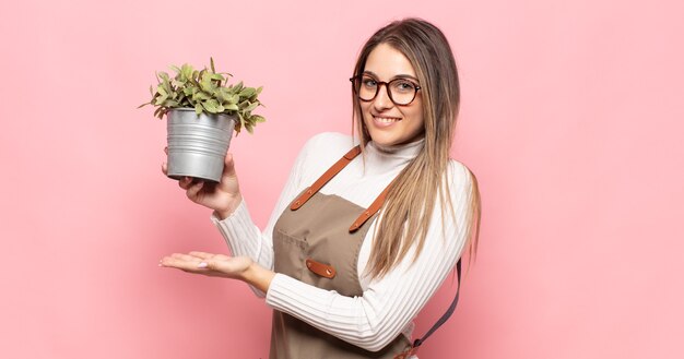 Joven mujer rubia sonriendo alegremente, sintiéndose feliz y mostrando un concepto en el espacio de la copia con la palma de la mano