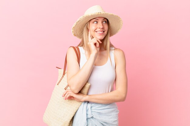 Joven mujer rubia sonriendo con una expresión feliz y segura con la mano en la barbilla