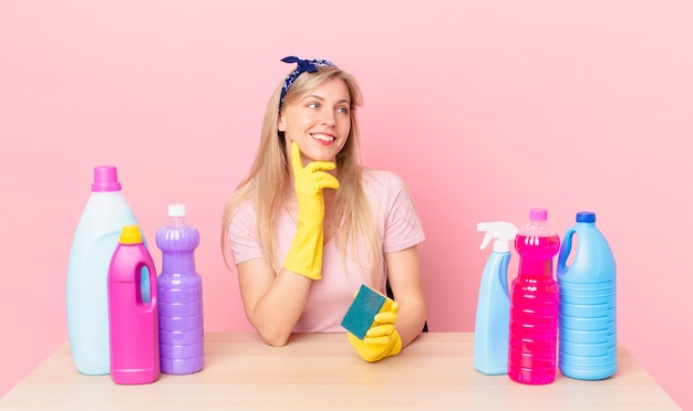 Joven mujer rubia sonriendo felizmente y soñando despierto o dudando. concepto de ama de llaves