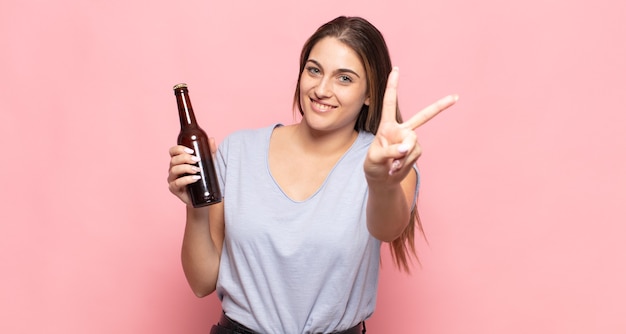 Foto joven mujer rubia sonriendo y luciendo feliz, despreocupada y positiva, gesticulando victoria o paz con una mano