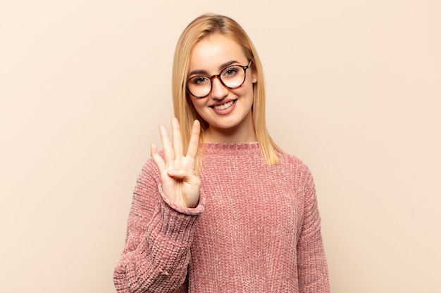 Joven mujer rubia sonriendo y mirando amistosamente, mostrando el número cuatro o cuarto con la mano hacia adelante, contando hacia atrás