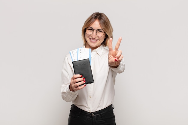 Joven mujer rubia sonriendo y mirando amistosamente, mostrando el número dos o el segundo con la mano hacia adelante, contando hacia atrás