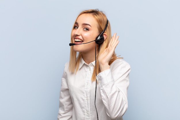 Joven mujer rubia sonriendo, mirando con curiosidad a un lado, tratando de escuchar chismes o escuchar un secreto