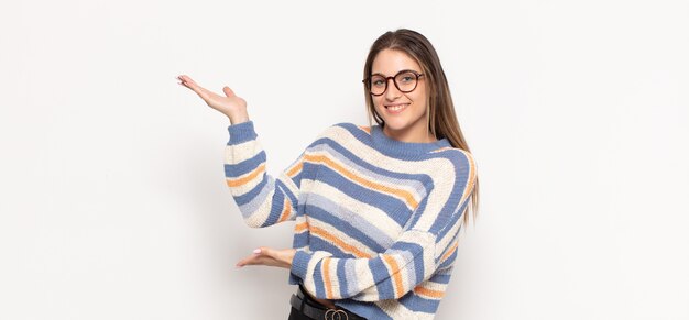 Joven mujer rubia sonriendo con orgullo y confianza, sintiéndose feliz y satisfecha y mostrando un concepto en el espacio de la copia