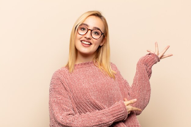 Joven mujer rubia sonriendo con orgullo y confianza, sintiéndose feliz y satisfecha y mostrando un concepto en el espacio de la copia