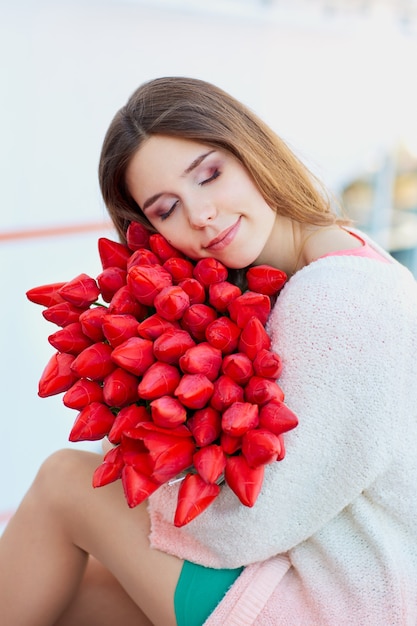 Joven mujer rubia sonriendo con un ramo de tulipanes rojos