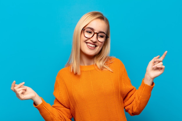 Joven mujer rubia sonriendo, sintiéndose despreocupada, relajada y feliz, bailando y escuchando música, divirtiéndose en una fiesta