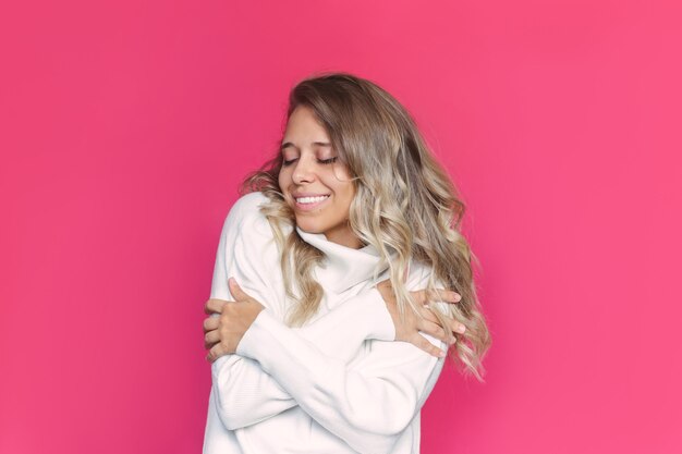 Una joven mujer rubia sonriente con cabello ondulado en un suéter de cachemira blanca disfruta de la suavidad