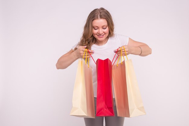 Joven mujer rubia sorprendida mira en la bolsa de compras en blanco