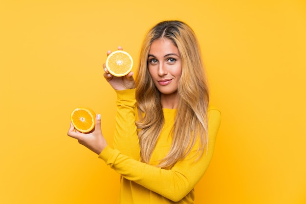 Joven mujer rubia sosteniendo una naranja sobre fondo amarillo