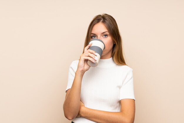 Joven mujer rubia sosteniendo y tomando un café para llevar